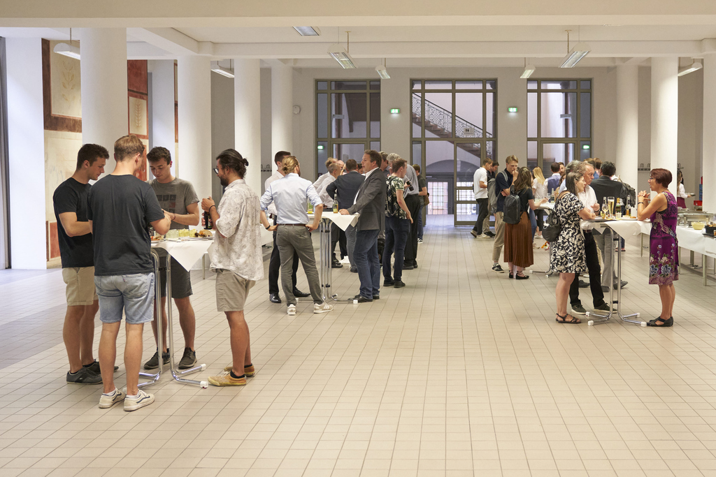 Menschen stehen in einer Halle bei einem Empfang zusammen und unterhalten sich.