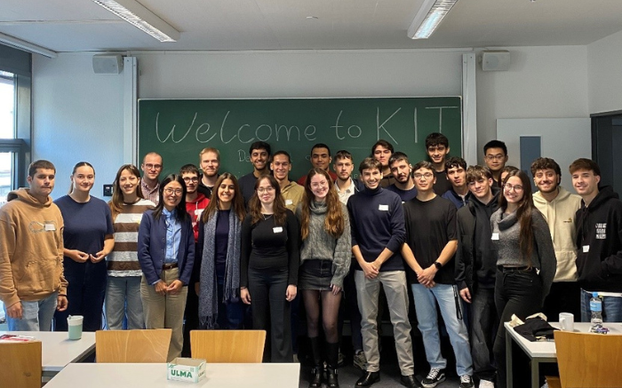 Studierende stehen vor einer Tafel im Seminarraum und lächeln in die Kamera